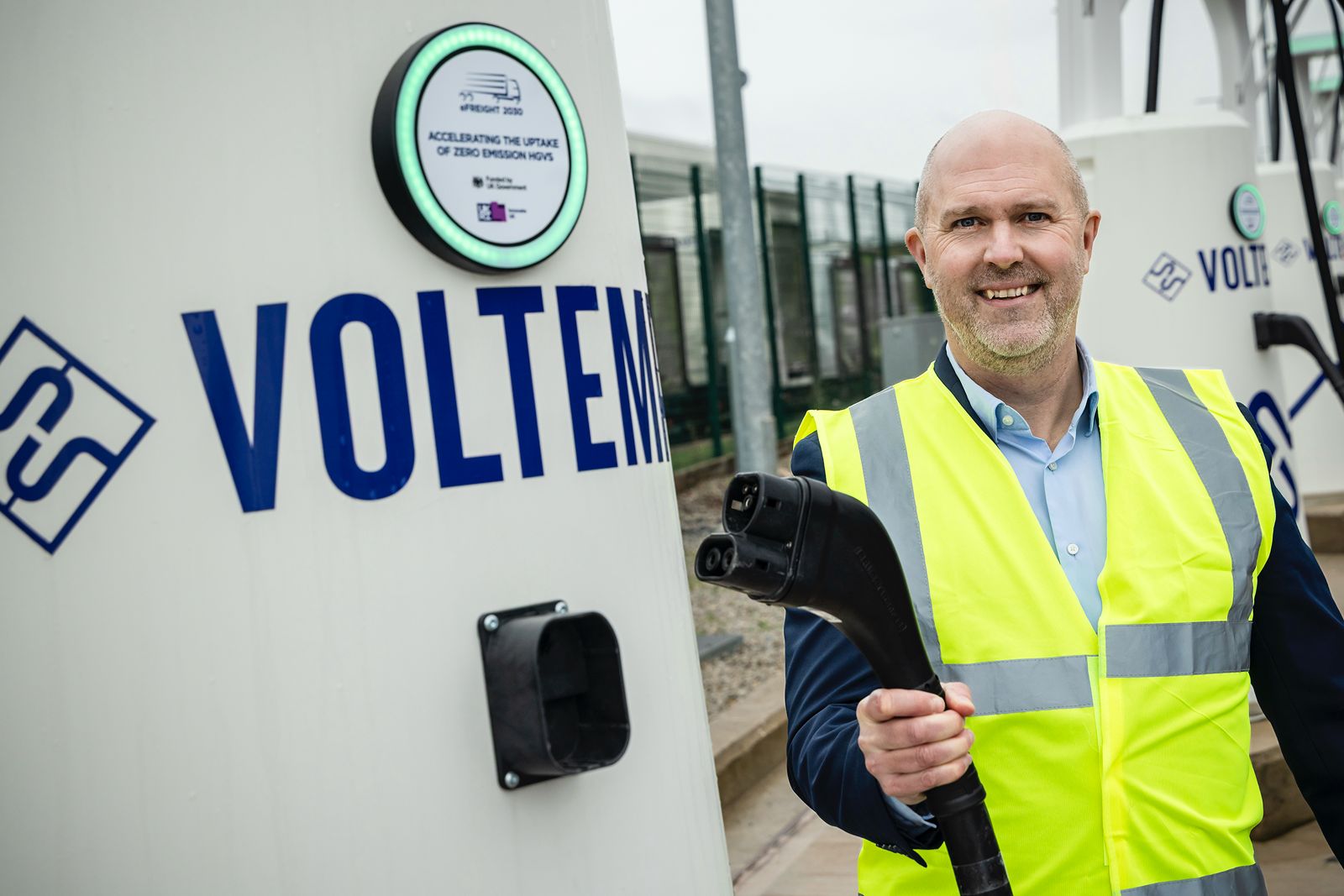 Voltempo CEO Simon Smith holding a Windrose E700 charging connector at a Voltempo HyperCharger unit
