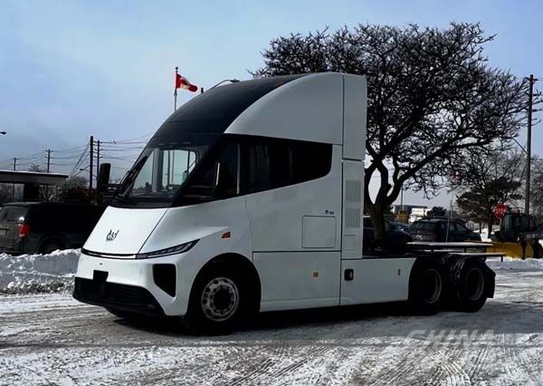 A Windrose electric truck parked in snow with a Canadian flag visible in the background